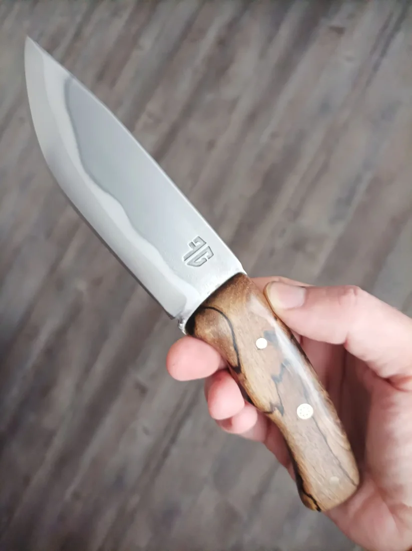 Couteau tenu en main, avec un manche en bois veiné et des rivets visibles.